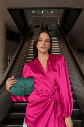 Donna con abito fucsia e borsa verde su una scala mobile, campagna Mirror, moda
